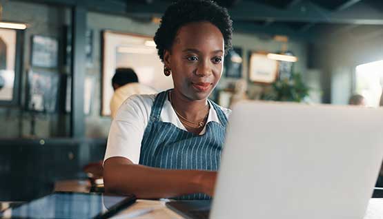 A business owner sits at one of her cafe tables withe her laptop to complete management tasks for the day.
